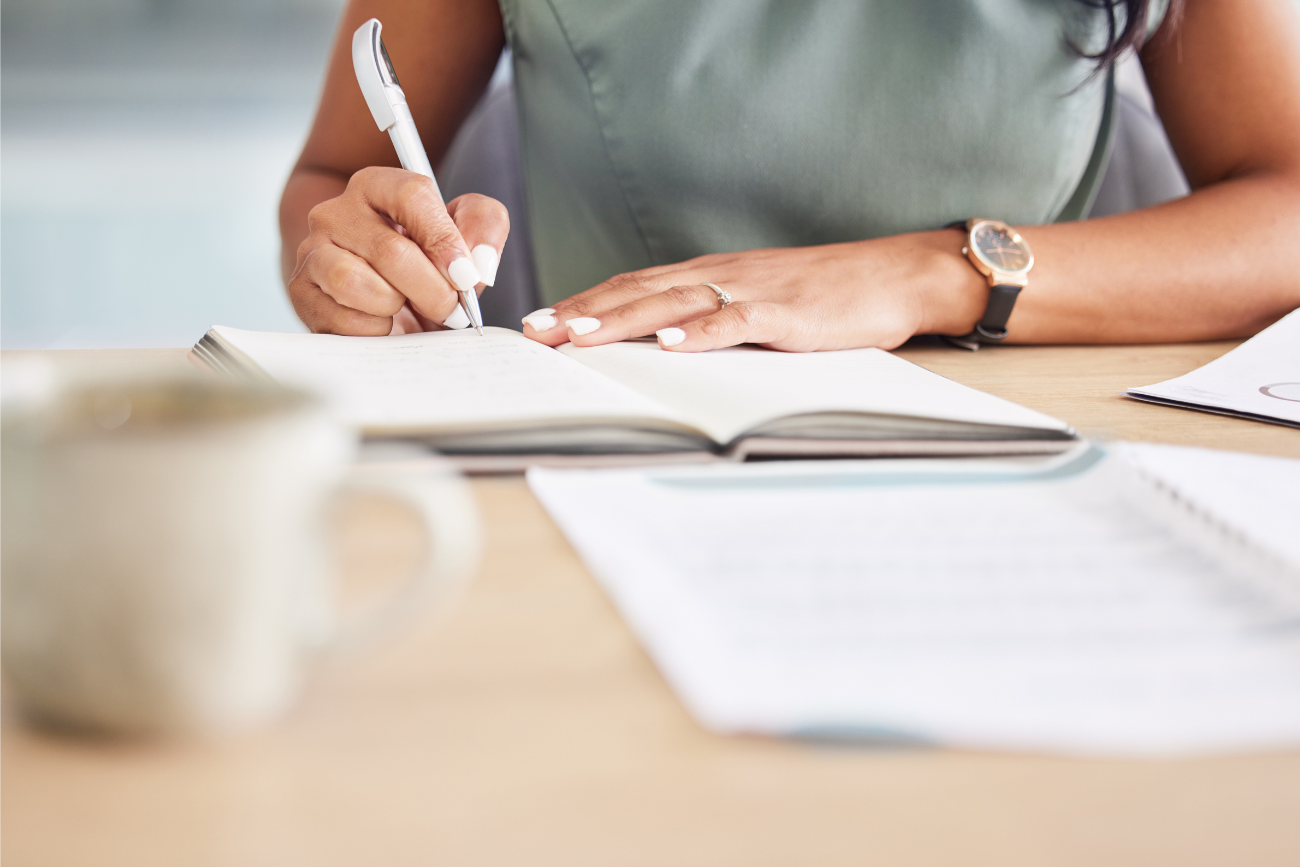 woman signing documents on desk with coffee cup